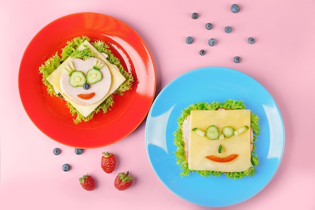 Photo red and blue plates with funny sandwiches on pink background