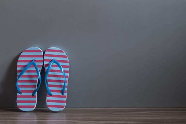 Red and Blue sandal shoes on wood floor against the grey wall. 