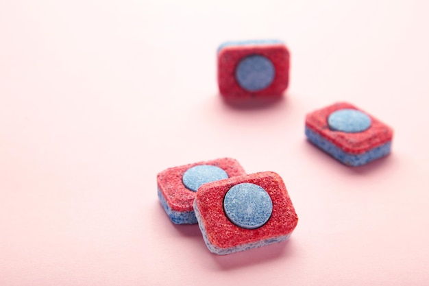 Red and blue tablets for dishwashing machine Detergents for home hygiene Dishwasher capsules on pink background Top view