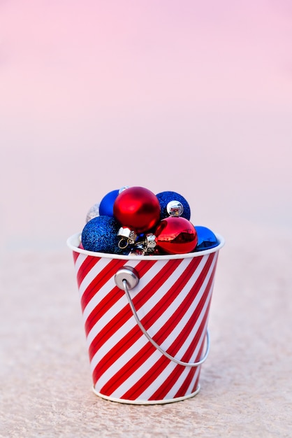 Palle rosse, blu e bianche raccolte nel secchio a strisce al tramonto per la decorazione di natale