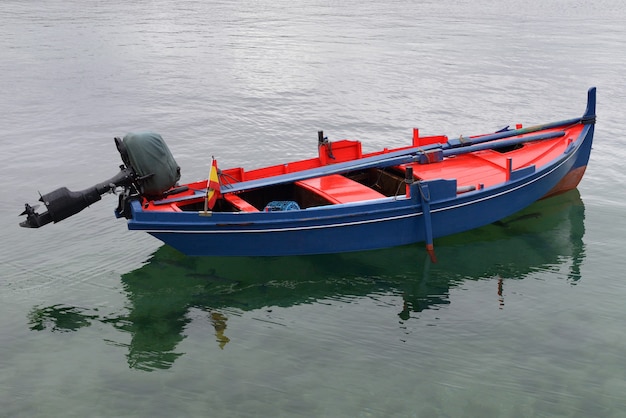 Red blue wooden fishing boat with motor moored in the sea