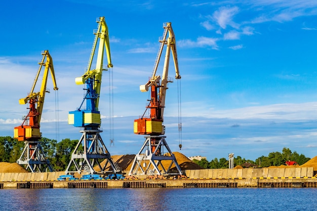 Red, blue and yellow cargo cranes stand on the banks of the\
venta river. ventspils, latvia, baltic