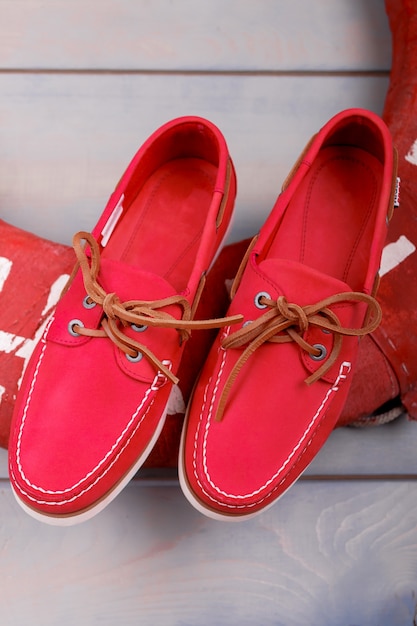 Photo red boat shoes on wooden background near lifebuoy. top view. close up.