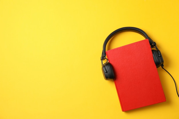 Red book with headphones on yellow background, top view