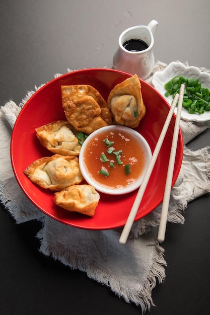 A red bowl of dumplings with a bowl of sauce and chopsticks