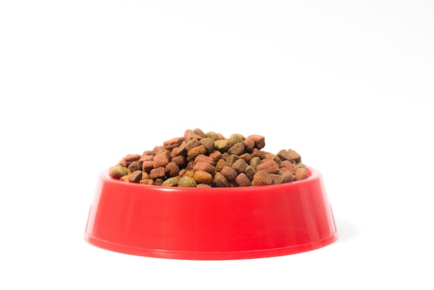 Red bowl with dry animal food for cats or dogs on white