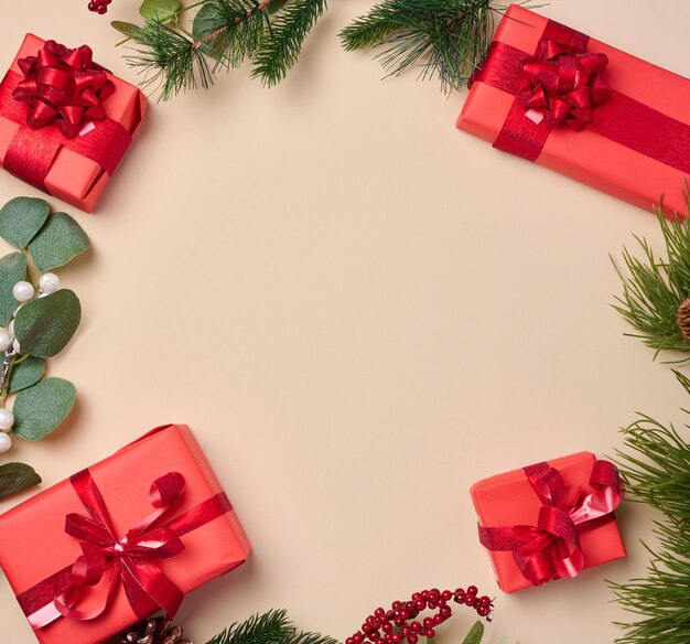 Red boxes with gifts fir branches with Christmas decor on a beige background erhu view Copy space