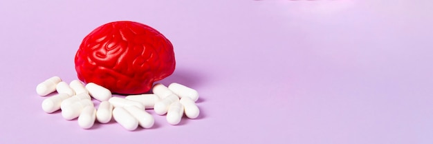 Photo red brain on a pink surface with white pills. brain pills. brain treatment.