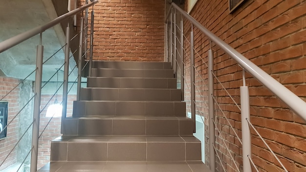 Red brick building with a modern staircase in a loft style with\
metal railing. stairs adorn the building. modern stairwell. steel\
railing. staircase in perspective.