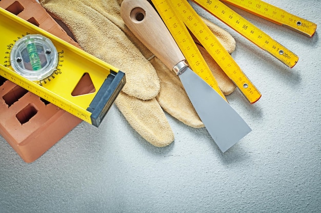 Red brick safety gloves paint scraper construction level wooden meter on concrete background bricklaying concept.