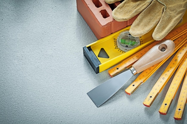 Foto guanti da lavoro in mattoni rossi intonacatura cazzuola livello di costruzione metro di legno su sfondo di cemento concetto di muratura