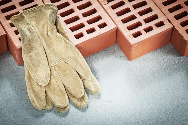 Red bricks leather protective gloves on concrete background construction concept.