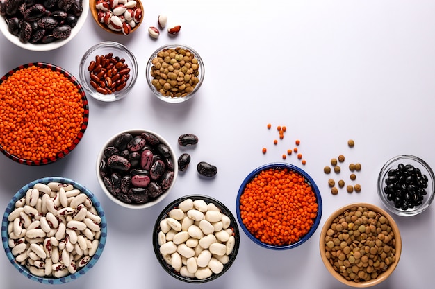 Red and brown lentils, black, brown and white beans are legumes that contain a lot of protein are located in bowls on white background