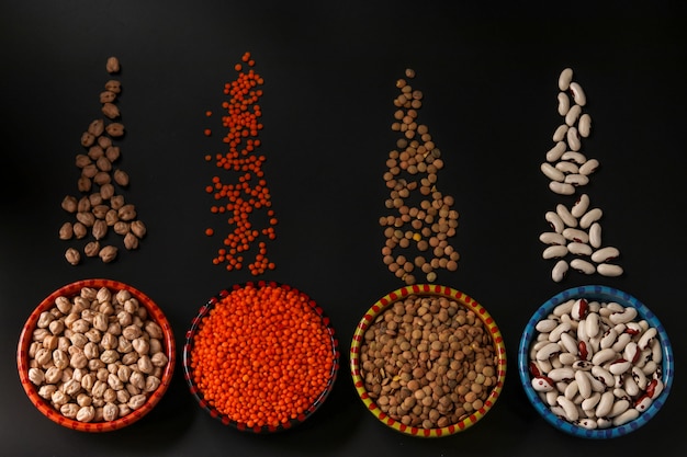 Red and brown lentils, chickpeas and white beans are legumes that contain a lot of protein are located on a dark background in bowls, horizontal orientation, top view