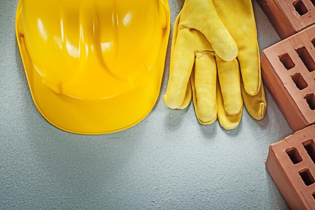 Red building bricks protective hard hat leather safety gloves on concrete surface construction concept.