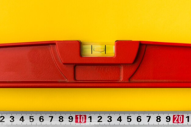 Red building level and tape measure on yellow background.