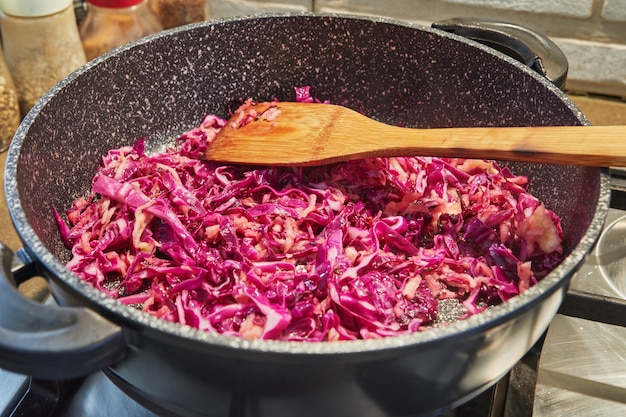 Red cabbage is fried in pan on gas stove.