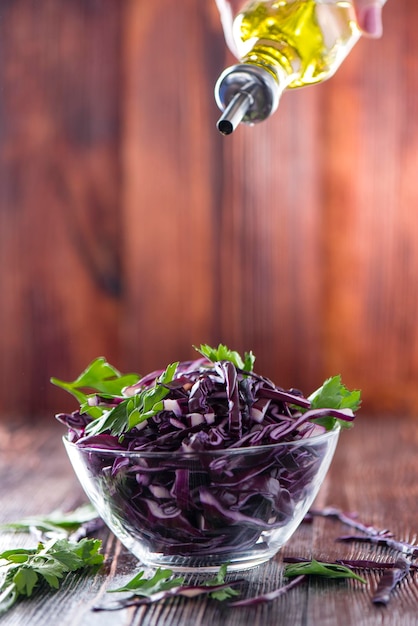 Red cabbage with parsley in a transparent bowl sprinkles a female hand with vegetable oil