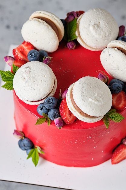 Red cake for a girl cake, decorated with macarons and fresh\
berries. cake for the holiday. dessert is decorated with fresh\
strawberries, blueberries and roses.