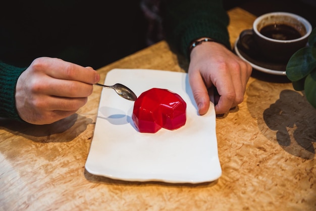 Red cake in the shape of a heart is on the table Mans hands with spoons stretch into a pie Valentines Day