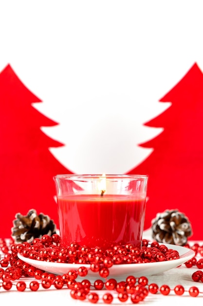 Red candle and felt christmas trees on white wooden table vertical