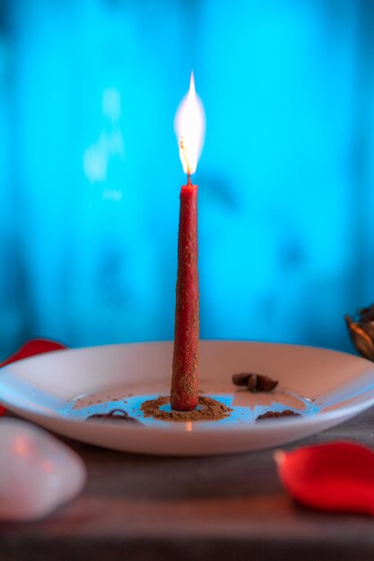 Photo a red candle lit on a blue background prepared with ground cinnamon with incense and rose quartz copy paste halloween spiritual beliefs white magic