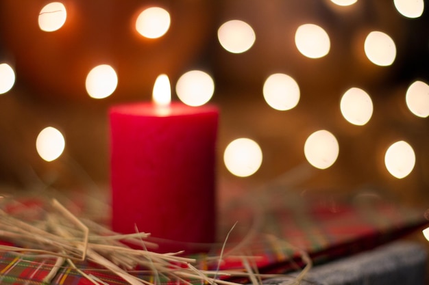 A red candle sits on a table with a few lights in the background.