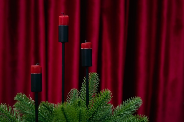 사진 인공 크리스마스 트리로 장식된 붉은 양초는 버건디 커튼이 있는 배경에 있습니다.