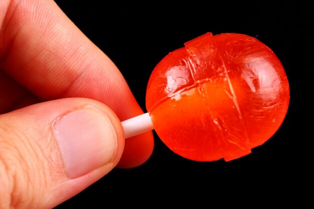 Red candy in hand on a stick on black surface