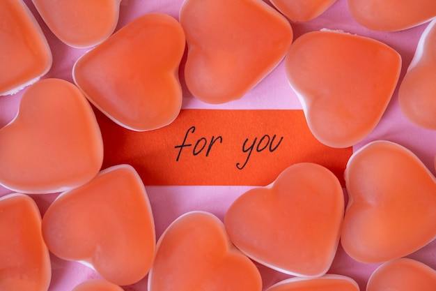 Red candy marmalade in shape of heart with a note FOR YOU on pink background Sugar gummy candy