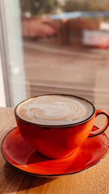 A red cappuccino cup on a cafe table against the background of a window