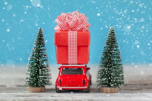 Red car carrying on roof a gift box  and Christmas tree. Christmas and New Year concept