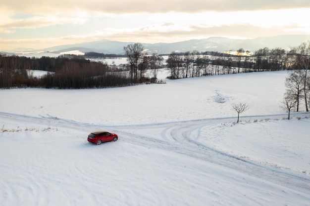 A red car drives along a snowy road