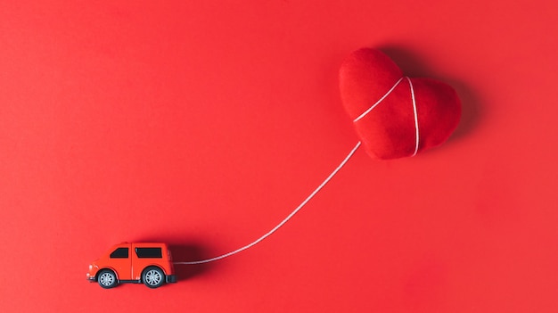 Foto un modello di auto rossa che rimorchia un cuscino cuore rosso su uno sfondo rosso, concetto, tema di san valentino