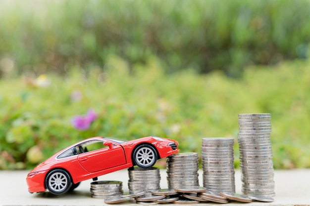 Photo red car on stack of coin on blurred green natural background. saving money and investment concept.