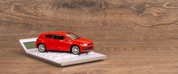 Red car and white calculator on wooden table, panoramic shot