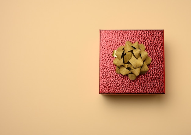 Red cardboard box tied with a silk red ribbon on a beige surface, top view