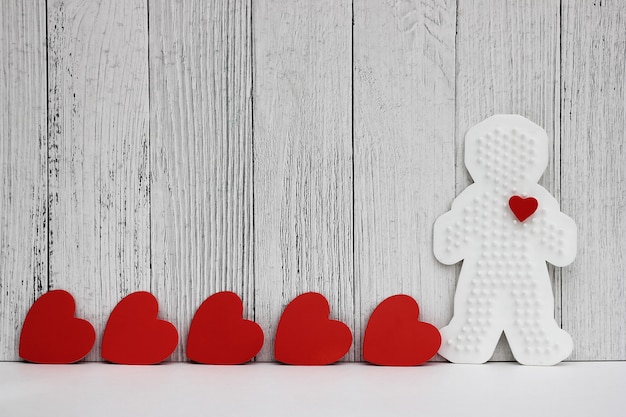 Red cardboard hearts are arranged in a row. Plastic figure of a man with a red heart. 