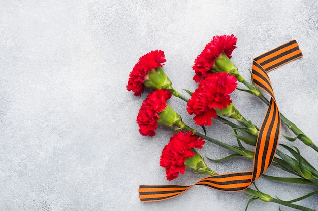 Red carnations and St. George ribbon on a concrete background.