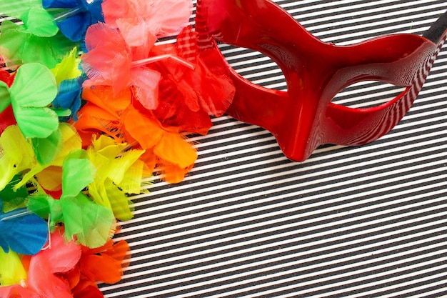 Red carnival mask on a black and white striped background and colorful flowers