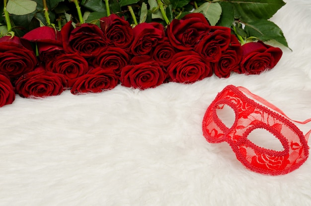 Red carnival mask lies  white fur in the  surface of a bouquet of roses