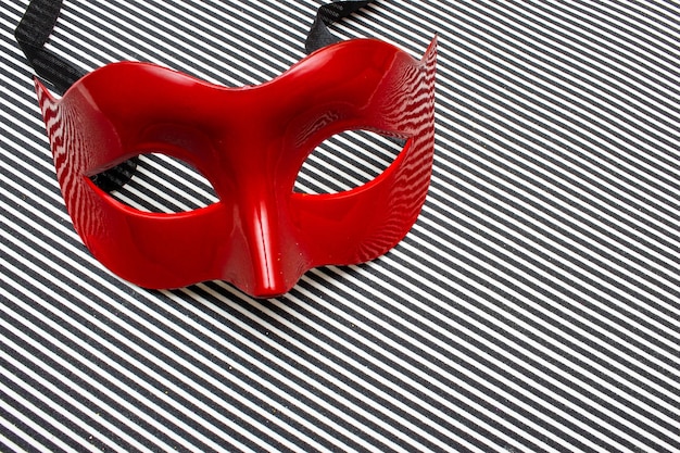 Фото Красная карнавальная маска на черно-белом полосатом фоне