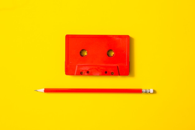Красная кассетная лента и карандаш на желтом фоне