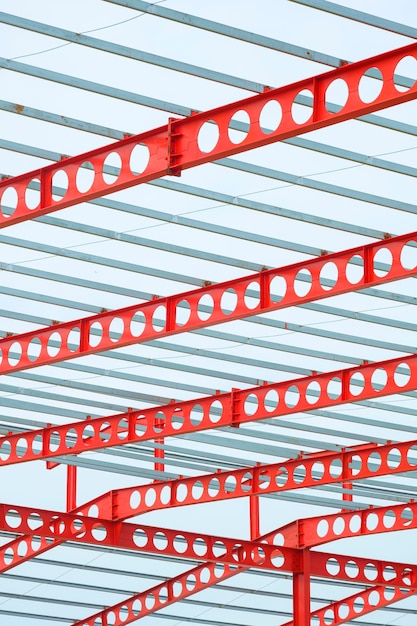 Red castellated beam metal roof structure of large industrial building in construction site