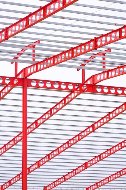 Red castellated beam metal roof structure of large industrial building in construction site