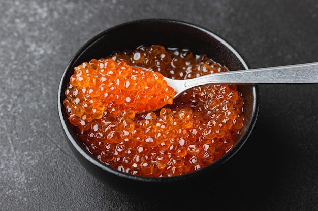 Red caviar in a black bowl with spoon