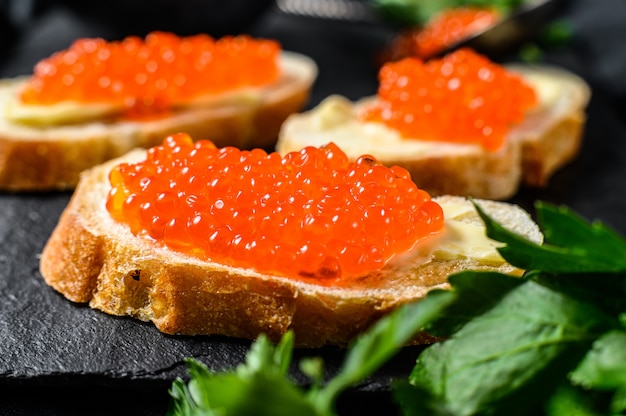 Red caviar in bowl and Sandwiches on stone board. Top view