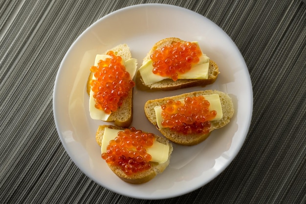 Red caviar on bread and butter closeup four sandwiches on white plate View from above