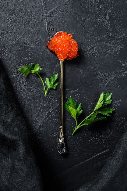 Red caviar in an exquisite spoon. Black background
