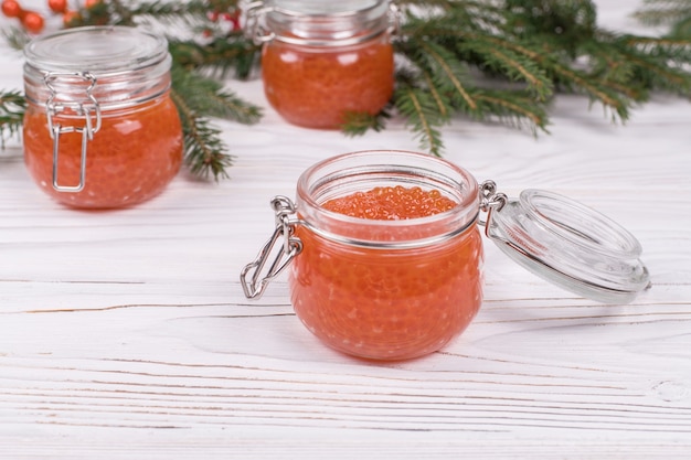 Red caviar in glass jar on aged white wooden table